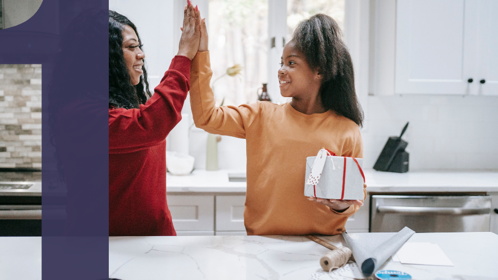 African American mother high-fiving daughter in the kitchen as they wrap a holiday gift