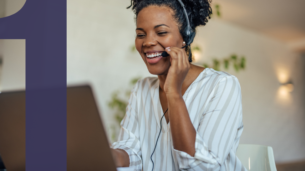 Smiling African American woman using headset to talk on the phone and using a laptop