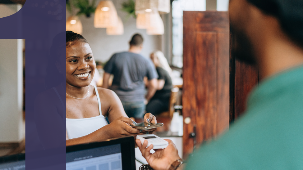 Smiling African American woman using phone for payment at a cafe